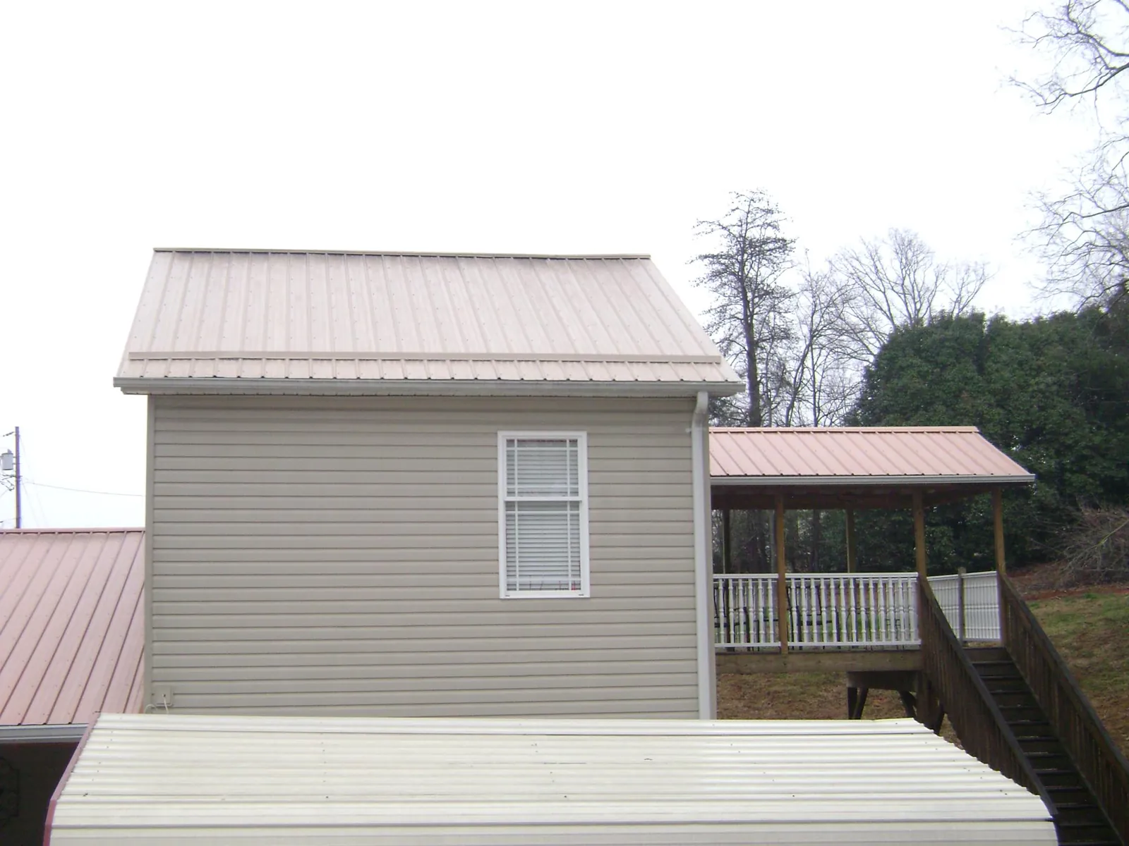 Tan metal roofs on a two story addition and attached porch, from a Roof Replacement job in Foster