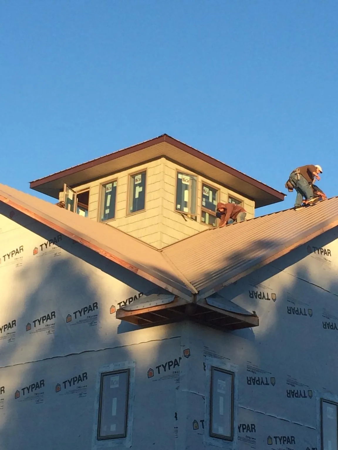 Roofers working around a rooftop cupola on a new metal roof at sunset — Roof Waterproofing in Foster by Roofing Brothers